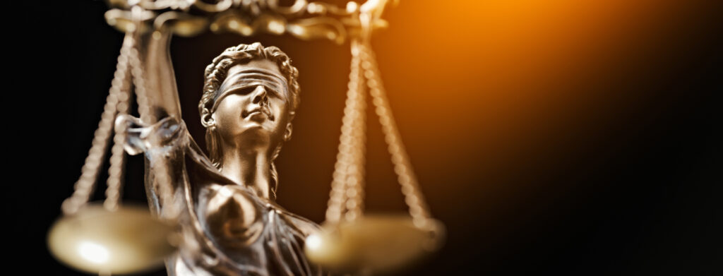 This image features the renowned statue of Justice, an embodiment of fairness and impartiality, often associated with law and legal proceedings. The statue is a powerful symbol in the context of arbitration, a method of resolving disputes outside the courts. The blindfolded figure holds balanced scales in one hand and a sword in the other, iconic elements that represent the equality and authority of justice. The image's focus on these symbols emphasises "arbitration" by highlighting the principles of unbiased judgement, balance, and equitable resolution that arbitration aims to achieve. The second aspect of this image is its dramatic lighting and composition that further underscore the concept of arbitration. The statue of Justice is illuminated against a darker background, drawing attention to its symbolic significance. The image composition is such that it places the statue - and therefore the idea of fair and impartial dispute resolution, at its very center. This creates a visual metaphor for the process of arbitration, where the goal is to attain justice outside of a traditional courtroom setting, embodied here by the prominent statue.